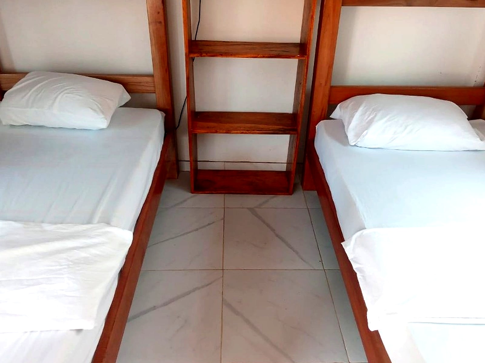 Habitación de madera con literas, sábanas blancas y estantería central